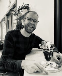 Gideon smiling at the camera, holding a plate with an ice cream sundae on top.